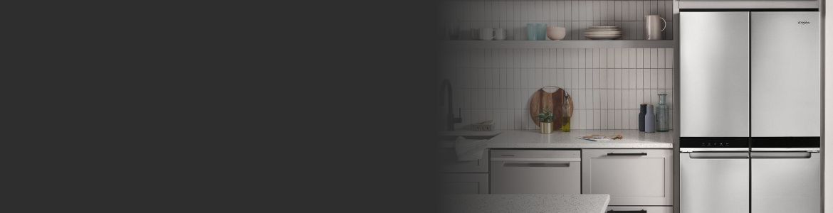 Une cuisine avec un lave-vaisselle Whirlpool. À côté, des comptoirs et une partie d'un réfrigérateur Whirlpool sont visibles. On trouve également dans la cuisine une planche à découper, des récipients à huile, une plante en pot, des assiettes et des tasses